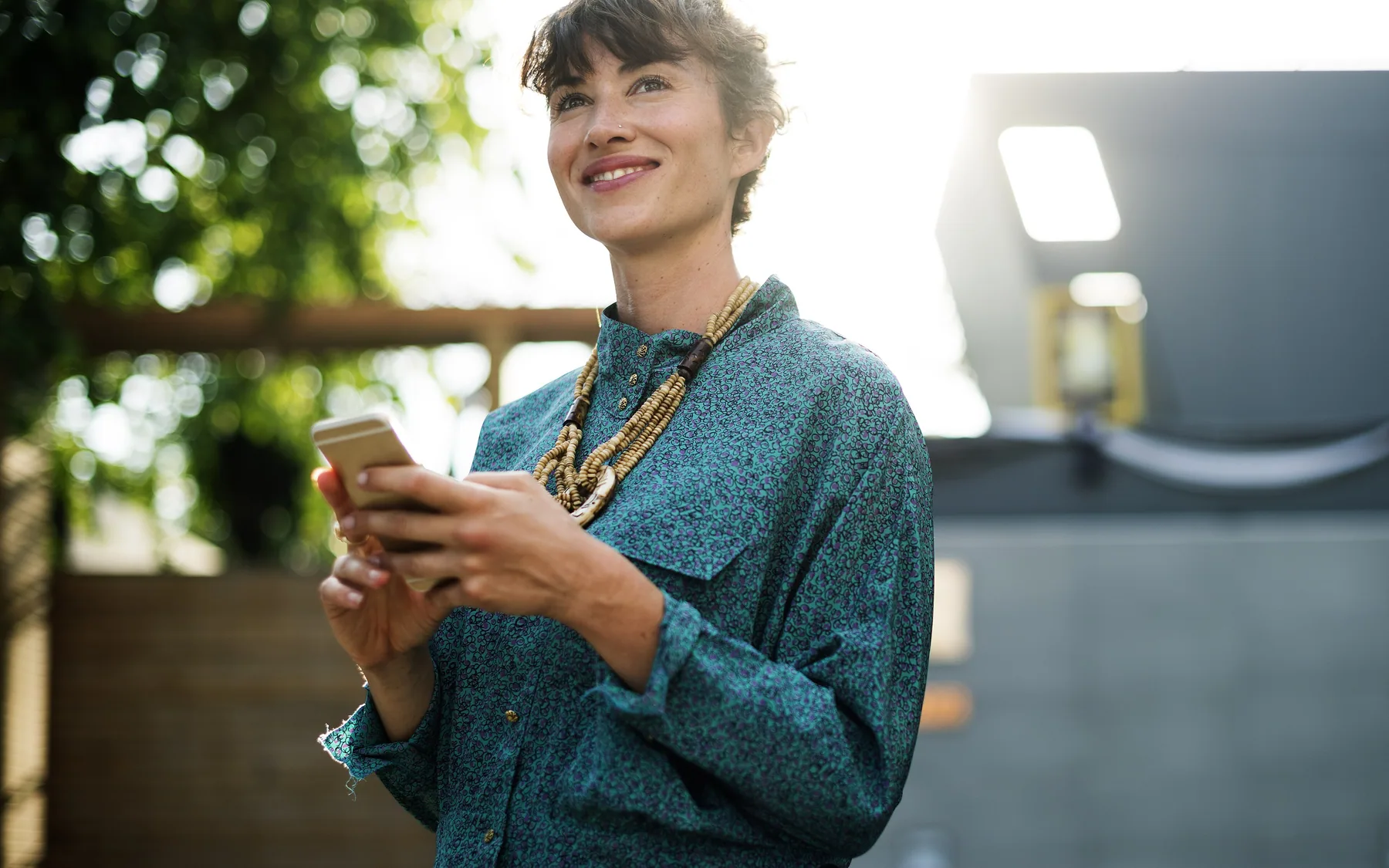 A person smiling at their phone outdoors in afternoon light