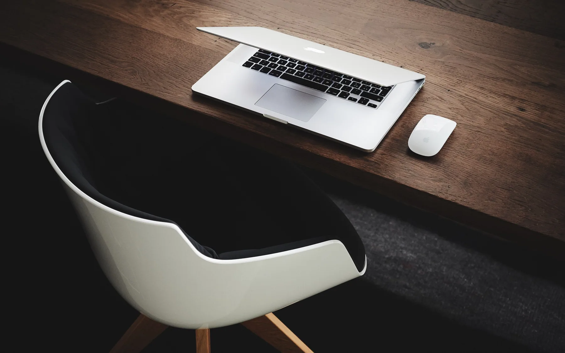 A laptop and mouse on a dark wooden desk beside a moulded chair